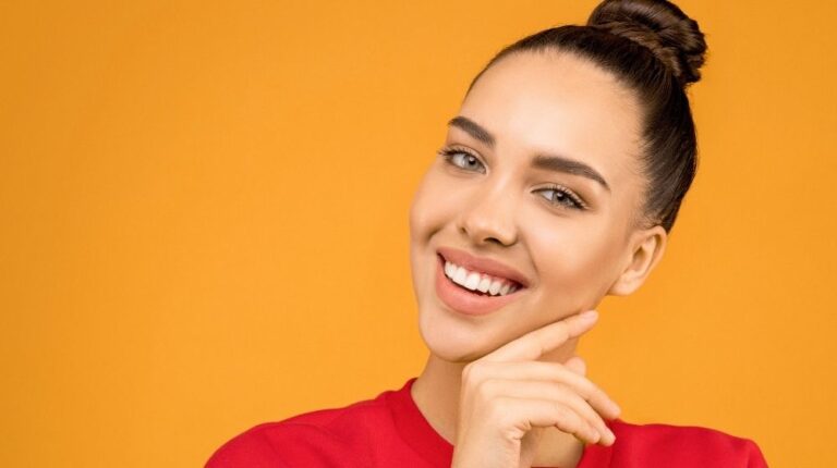 woman in red shirt with orange background | How To Curl Your Eyelashes Without A Curler | Featured